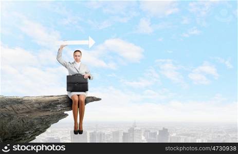 Businesswoman with arrow. Young businesswoman sitting on top of cliff