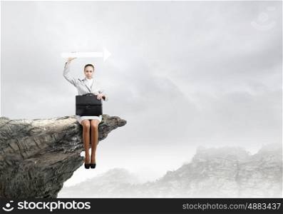 Businesswoman with arrow. Young businesswoman sitting on top of cliff