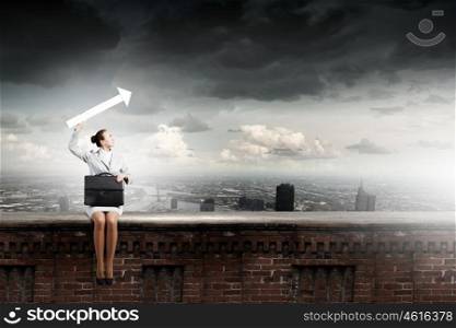 Businesswoman with arrow. Young businesswoman with suitcase sitting on top of building