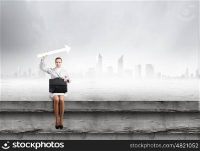 Businesswoman with arrow. Young businesswoman with suitcase sitting on top of building