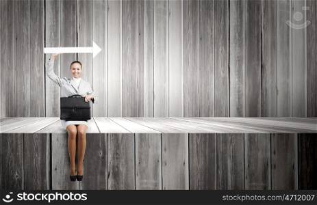 Businesswoman with arrow. Young businesswoman with suitcase sitting on wooden surface