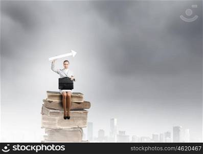 Businesswoman with arrow. Young pretty businesswoman sitting on pile of books