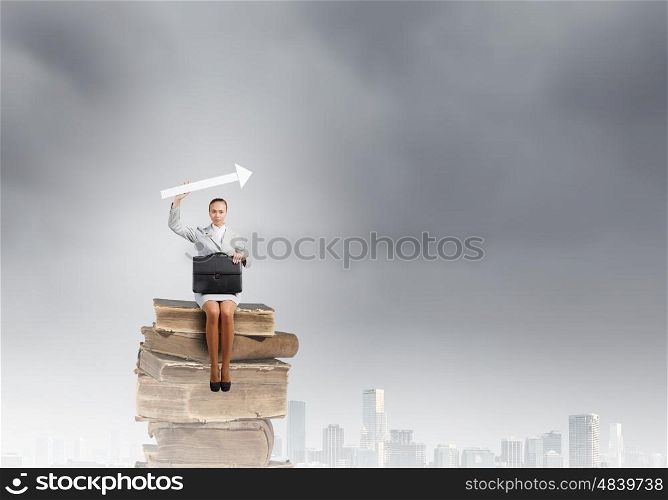 Businesswoman with arrow. Young pretty businesswoman sitting on pile of books