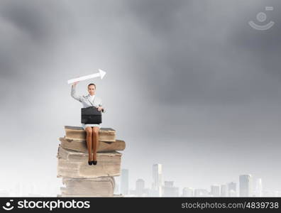 Businesswoman with arrow. Young pretty businesswoman sitting on pile of books