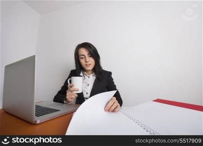 Businesswoman with coffee mug reading documents at desk in office