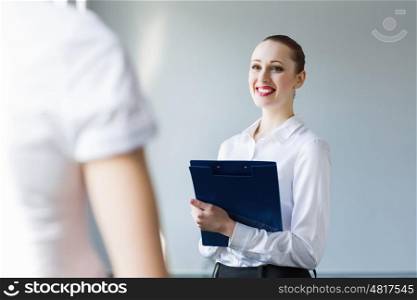 Businesswoman with colleague. Image of young businesswoman holding folder and talking to colleague