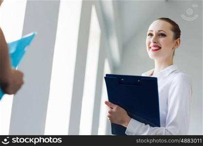 Businesswoman with colleague. Image of young businesswoman holding folder and talking to colleague