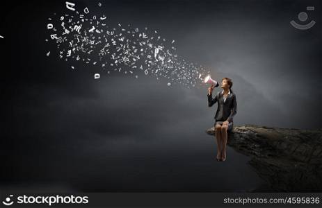 Businesswoman with megaphone. Young businesswoman sitting on rock edge and screaming in megaphone