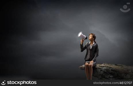 Businesswoman with megaphone. Young businesswoman sitting on rock edge and screaming in megaphone