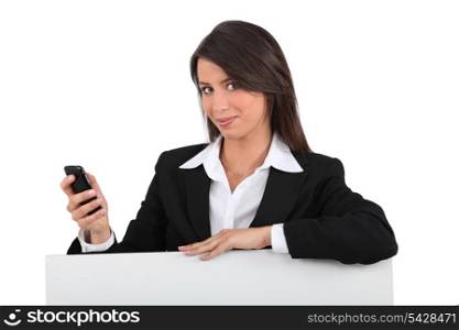 Businesswoman with mobile posing by blank poster
