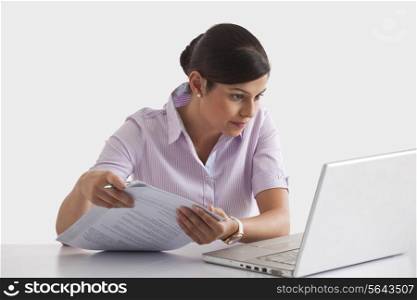 Businesswoman with paperwork looking at laptop screen
