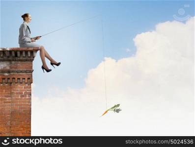 Businesswoman with rod. Young businesswoman sitting on top of building and fishing
