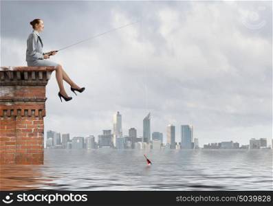 Businesswoman with rod. Young businesswoman sitting on top of building and fishing