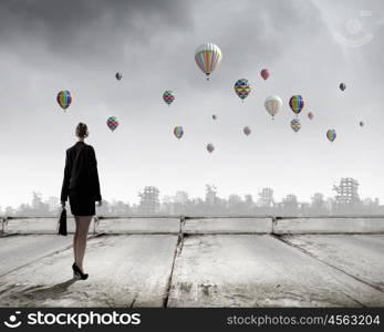 Businesswoman with suitcase. Rear view of businesswoman looking at aerostats flying above city