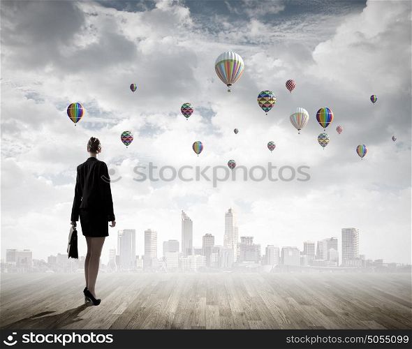 Businesswoman with suitcase. Rear view of businesswoman looking at aerostats flying above city