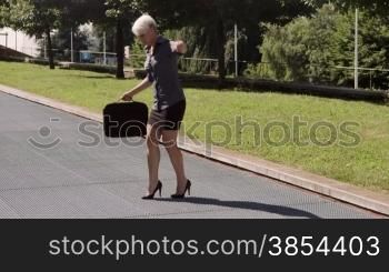 Businesswoman with suitcase trying to find balance on high heels on grating and having difficulties walking with fashion shoes. Sequence