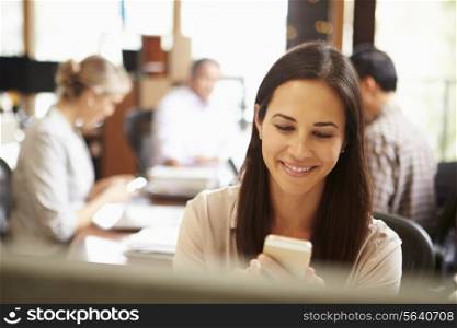 Businesswoman Working At Desk Using Mobile Phone