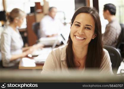 Businesswoman Working At Desk With Meeting In Background