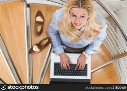 Businesswoman working at home with her laptop sitting on the stairs in her apartment