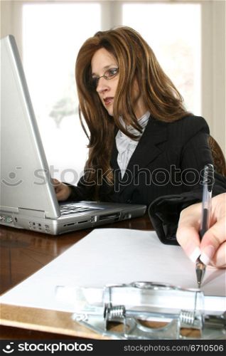 Businesswoman working on a laptop and writing on a clipboard