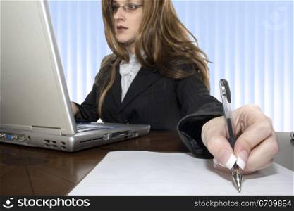 Businesswoman working on a laptop and writing on a sheet of paper