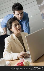 Businesswoman working on a laptop with another businessman standing behind her