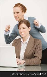 Businesswoman working on a laptop with her colleague clenching teeth behind her