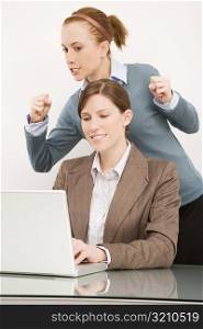 Businesswoman working on a laptop with her colleague clenching teeth behind her