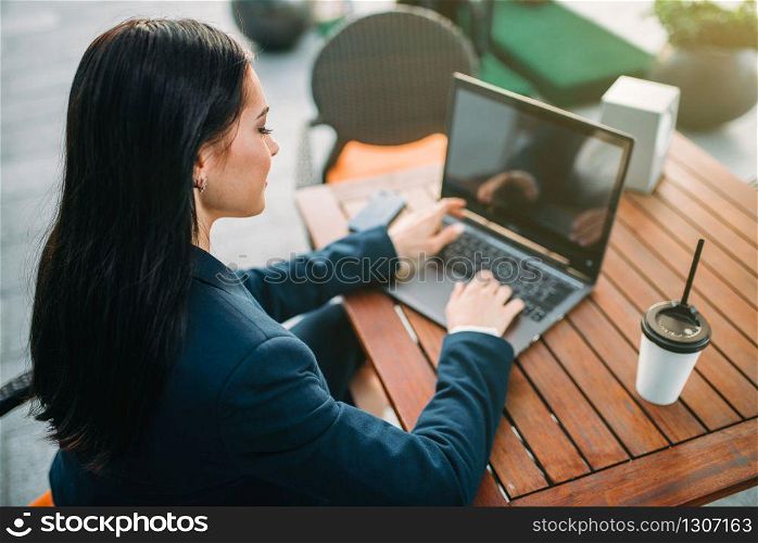 Businesswoman works on laptop in office, top view. Modern building, financial center, cityscape. Female businessperson in suit at workplace