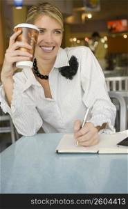 Businesswoman writing in a diary and smiling in a restaurant