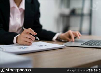 Businesswoman writing notes on document and typing data on laptop about marketing plan of startup.