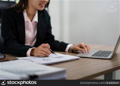 Businesswoman writing notes on document and typing data on laptop about marketing plan of startup.