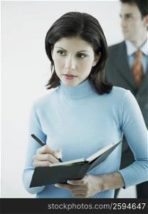 Businesswoman writing on a personal organizer with a businessman standing behind her