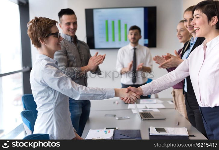 businesswomans handshake on team meeting with group of people blured in background at modern startup business office interior