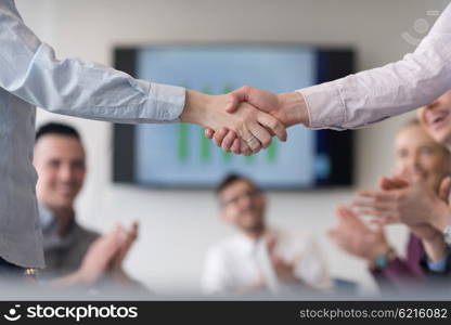 businesswomans handshake on team meeting with group of people blured in background at modern startup business office interior