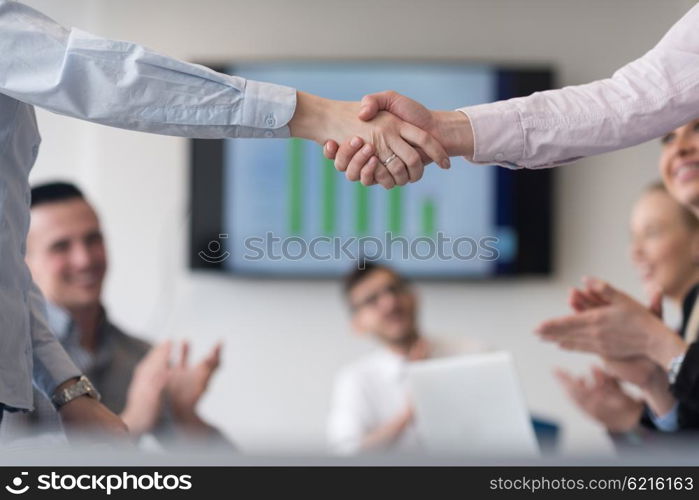 businesswomans handshake on team meeting with group of people blured in background at modern startup business office interior