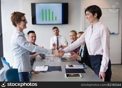 businesswomans handshake on team meeting with group of people blured in background at modern startup business office interior