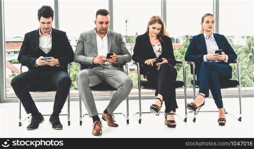 Businesswomen and businessmen using mobile phone while waiting on chairs in office for job interview. Corporate business and human resources concept.