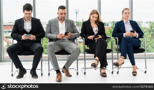 Businesswomen and businessmen using mobile phone while waiting on chairs in office for job interview. Corporate business and human resources concept.
