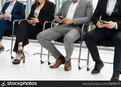 Businesswomen and businessmen using mobile phone while waiting on chairs in office for job interview. Corporate business and human resources concept.