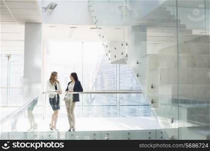 Businesswomen conversing against railing in office