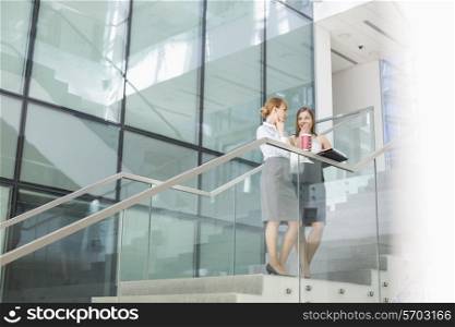 Businesswomen conversing while having coffee on steps in office