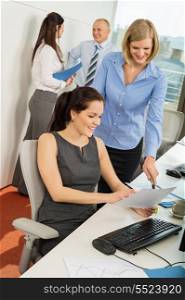 Businesswomen discussing document with colleagues in background at office