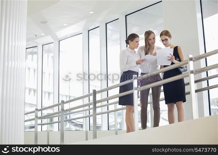 Businesswomen discussing over paperwork against railing
