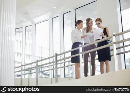 Businesswomen discussing over paperwork against railing