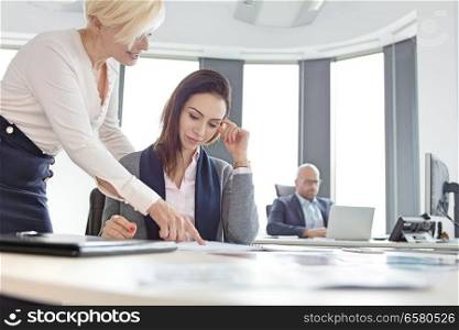 Businesswomen discussing over project with male colleague in background at office