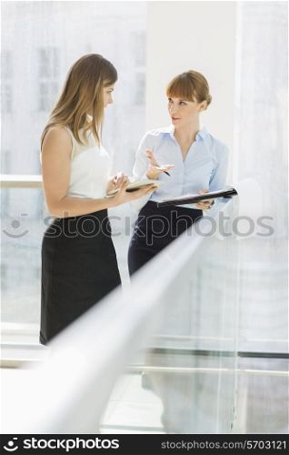 Businesswomen discussing while standing by railing in office