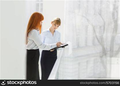 Businesswomen doing paperwork while standing by railing in office