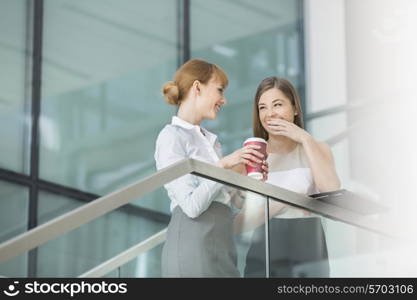 Businesswomen gossiping while having coffee on steps in office