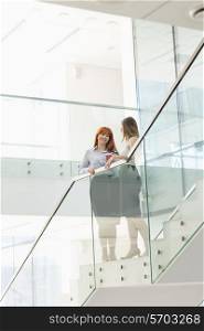 Businesswomen having coffee while standing on steps in office